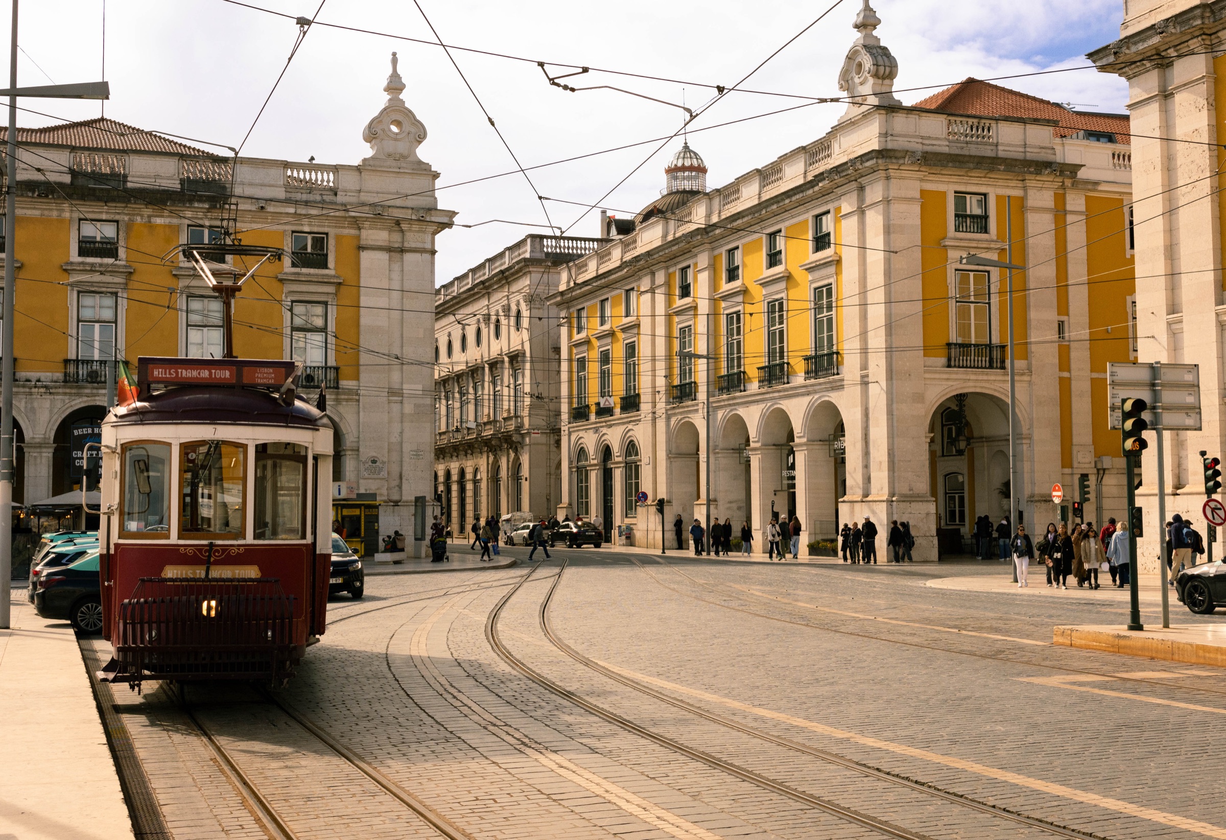 Elétrico antigo a passar por edifícios arcados na Praça do Comércio, Lisboa