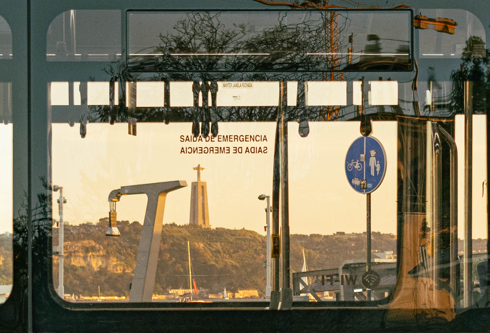 Reflexo do Cristo Rei na janela de um elétrico ao pôr do sol, Lisboa