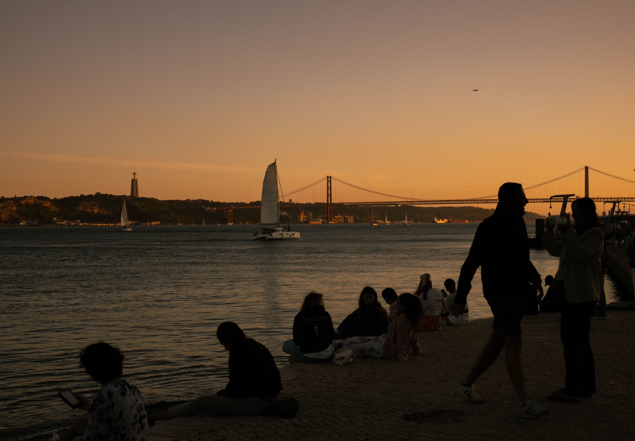 Silhuetas junto ao Tejo ao pôr do sol, com a Ponte 25 de Abril