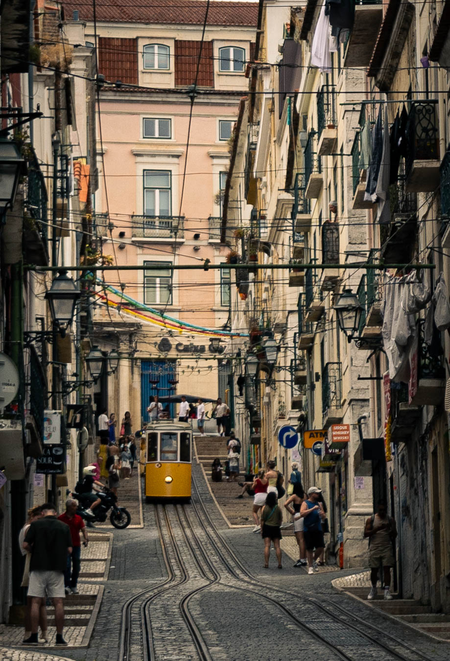 Elétrico amarelo a subir uma rua decorada na Bica, Lisboa